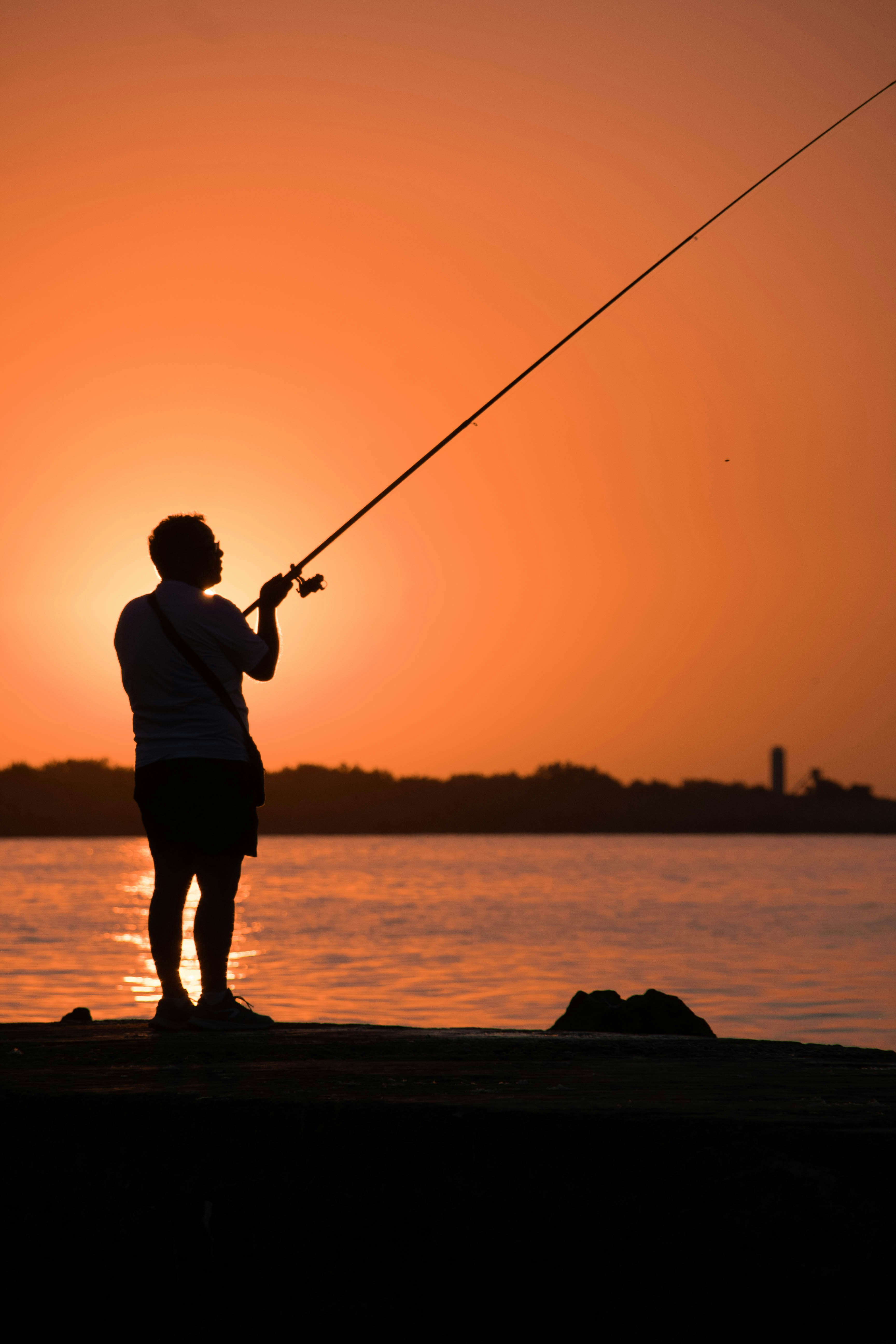 silhouette of man fishing on sea during sunset